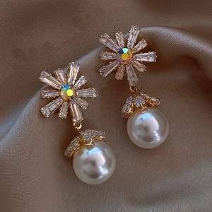 Detailed view of floral gold earrings with crystals and a large white pearl drop