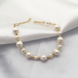 Detailed macro view of baroque freshwater pearl bracelet with gold beads on white silk