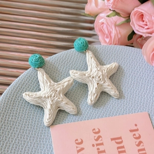 Detail of woven raffia star earrings with blue bead on a decorative tray