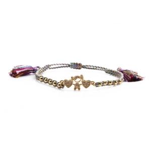 Detail of woven bracelet with gold heart charm and colorful tassel on white background