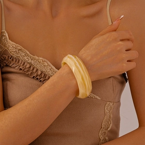 Close-up of a wide amber acrylic bangle with marble texture worn by a fashion model