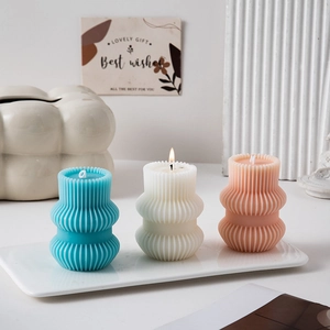 Three geometric pillar scented candles in blue, white and pink with vertical stripes