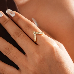 Macro close-up of a gold V-shaped ring with pave-set crystals on a model's finger