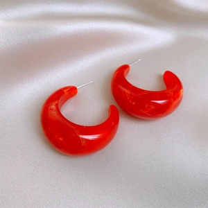 Macro shot of bright red C-shaped resin earrings on soft beige satin fabric