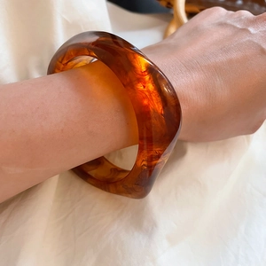 Close-up of wide amber acrylic resin bangle showing natural marbled pattern on wrist