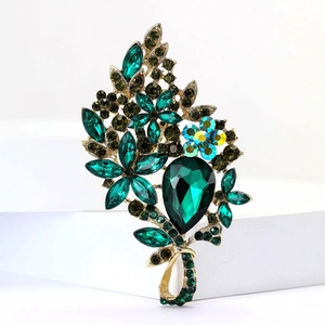 Detailed close-up of a floral alloy brooch with green crystals on a white background