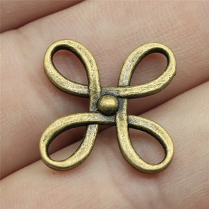 Macro shot of a bronze Chinese knot jewelry connector charm on a fingertip for scale