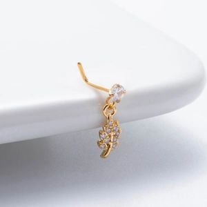 Close-up of gold L-shaped nose stud with leaf zircon pendant on a white surface
