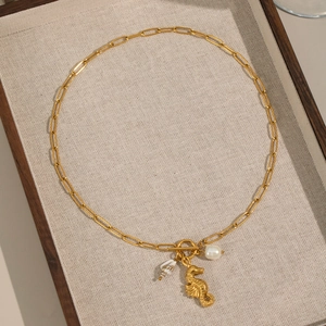 Detail of 18K gold seahorse and pearl pendants on a paperclip chain in a wooden tray