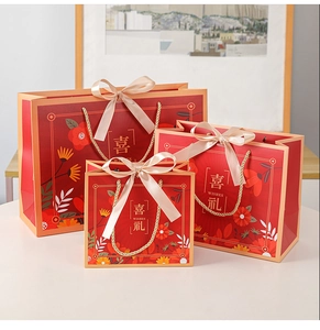 Three sizes of red Chinese gift bags with gold handles and pink ribbons in a tiered layout