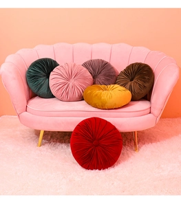 Velvet round pumpkin floor pillows in multiple colors displayed on a modern pink sofa