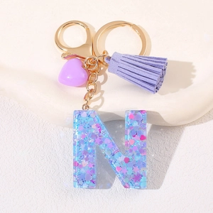 Detailed shot of resin letter N keychain with purple heart charm and soft fringe tassel