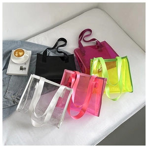 Detail of colorful transparent PVC tote bags in multiple colors on a bed with lifestyle props
