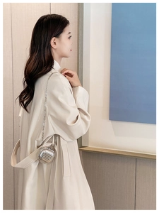 Close-up of a silver striped mini crossbody bag with metal chain on a beige coat