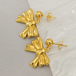 Macro detail of high-polished 18K gold-plated bow stud earrings on textured white surface