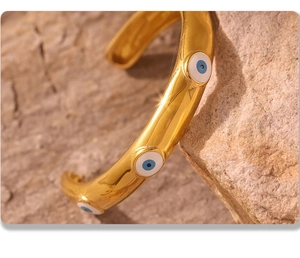 Detail of gold evil eye open cuff bracelet resting on a textured stone surface