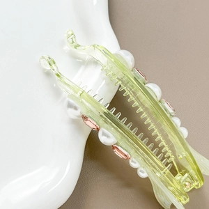 Green resin banana hair clip with pearls and pink rhinestones on a textured background