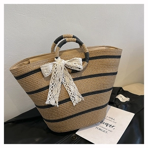 Detail of woven straw basket bag with black stripes and large white lace bow