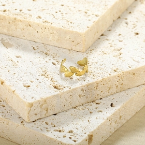 Gold leaf-shaped minimalist open ring displayed on beige natural stone surface