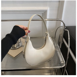 Detail of cream-colored half-moon underarm bag with silver buckle on a steel shelf