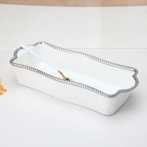 Close-up of a white rectangular ceramic plate with silver beaded edges and gold spoon