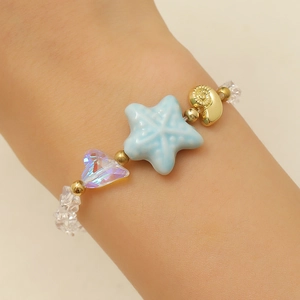 Close-up of ocean-style bracelet with blue starfish, gold shell, and heart beads
