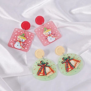 Detail of Christmas snowman and bell acrylic earrings on elegant white satin fabric