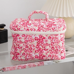 Quilted floral makeup bag with top handle and zipper closure on a glass table