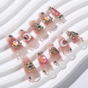 Detail of pink press-on nails with pearls, rhinestones, and golden moon accents