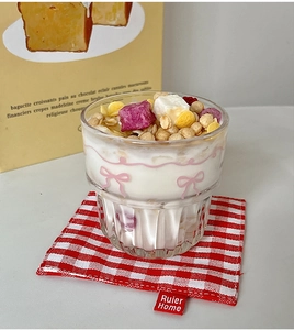 Detail of clear glass cup with pink bow design holding yogurt and granola on a red coaster