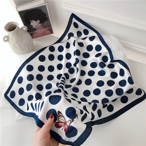 Detailed view of white silk scarf with blue polka dots and artistic butterfly pattern