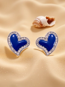 Macro detail of heart earrings with blue zirconia and silver plating on silk background