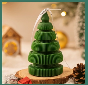 Close-up of a green origami Christmas tree scented candle with silk ribbon on a wood base