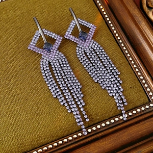 Macro shot of geometric lavender crystal earrings with dangling tassel on olive fabric