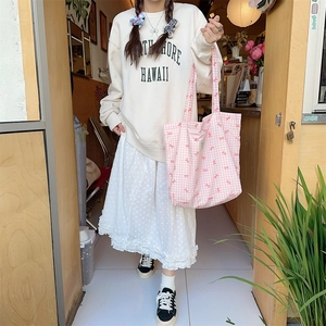 Detail view of pink plaid canvas tote bag paired with floral skirt and casual hoodie