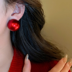 Close-up of a model wearing large glossy red round pearl earrings with red sweater