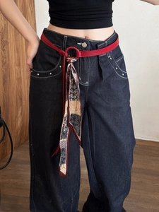 Detail of red leather belt with vintage floral silk scarf on dark blue jeans