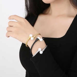 Three twisted wire cuff bracelets in gold, silver, and black with double pearls on model