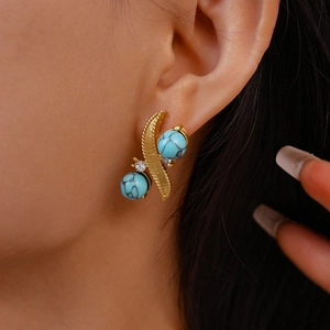 Detailed close-up of a gold leaf earring with turquoise beads and sparkling rhinestones