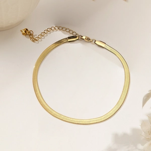 Elegant 18k gold flat snake chain bracelet with heart pendant on a soft beige surface