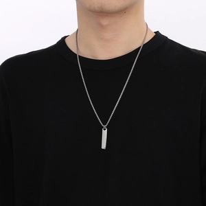 Close-up of a silver rectangular bar pendant on a braided chain worn by a male model