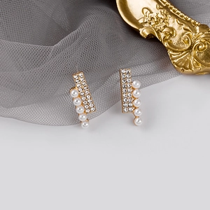 Macro detail of gold-plated earrings with pearls and crystals on grey mesh background