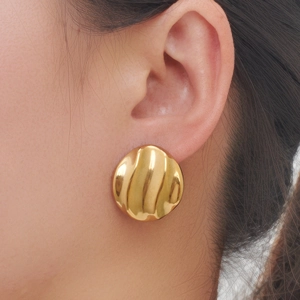 Nahaufnahme eines großen goldenen Edelstahl-Ohrrings mit Wellenstruktur an einem Model