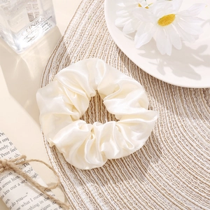 Detail view of cream satin scrunchie on woven mat with vintage aesthetic props