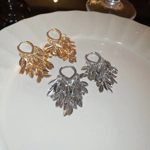 Close-up detail of tiered leaf tassel earrings in gold and silver on a white ceramic plate