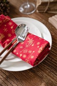 Détail d'une serviette de Noël rouge aux flocons dorés avec couverts sur une table en bois