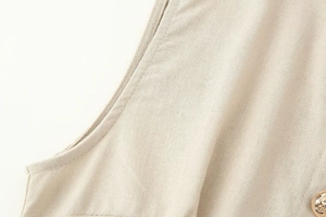 Dettaglio di abito midi beige in lino con trama del tessuto, cuciture e bottone in metallo