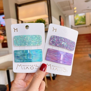 Hand holding holographic laser hair clips in green, blue and purple on cards