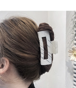Detail showing a white marble pattern hair claw clip holding a brunette bun hairstyle