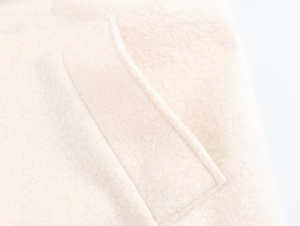 Detailed macro view of the cream wool blend fabric and stitching quality of the overcoat